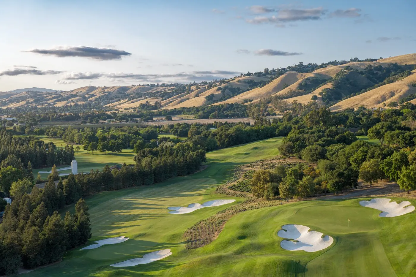 An aerial view of The Institute at golden hour, with bunkers and oaks below the hills