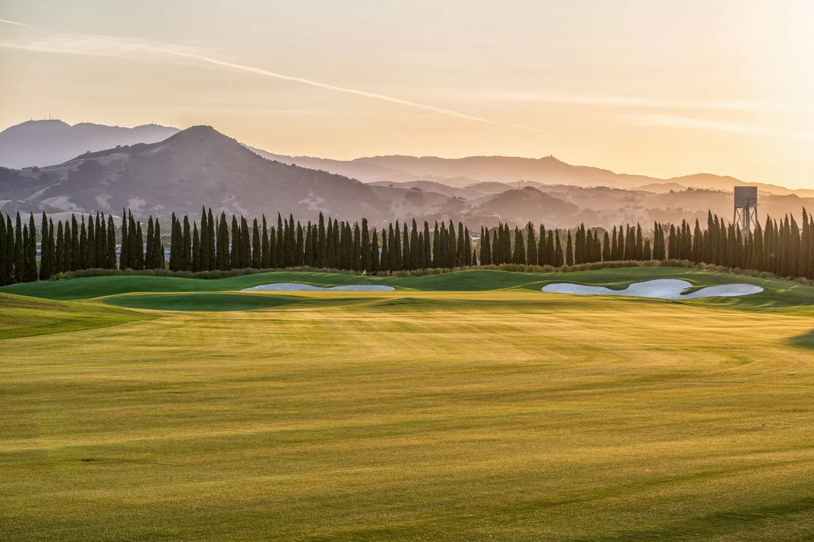 The Institute Golf Club at sunset, with cypress trees and mountains beyond the fairway